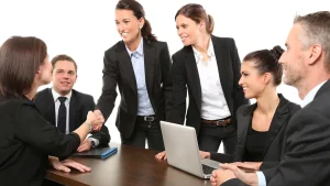 Business team shaking hands across a meeting table with a laptop