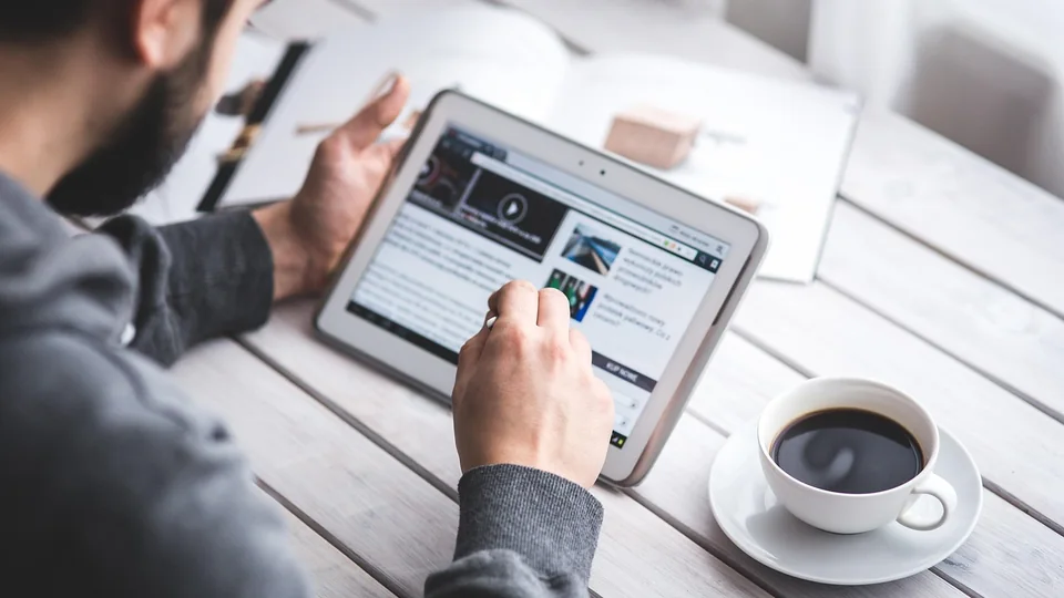 Person reading a web page on a tablet at a desk with a cup of coffee