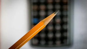 Sharpened yellow pencil in front of a blurred calculator on a desk